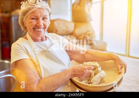 Bonne femme âgée comme boulanger expérimenté pétrir de la pâte dans une boulangerie familiale Banque D'Images