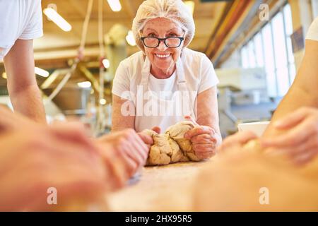 Femme âgée en tant que patron senior pétrir la pâte comme un travail d'équipe dans la boulangerie familiale Banque D'Images