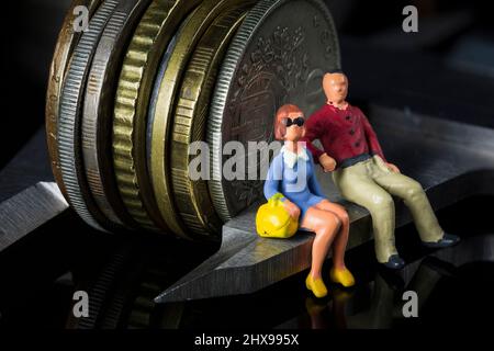 Personnes miniatures: Jeune couple assis sur pied à coulisse mesurant la pile de pièces. Planification de la retraite. Économies d'argent et investissements. Compte à rebours Banque D'Images