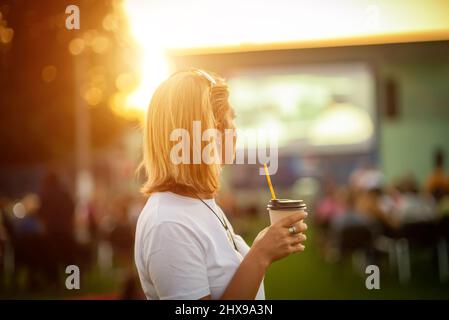 Cinéma en plein air. Fille avec un verre de café regardant un film dans un cinéma d'été Banque D'Images