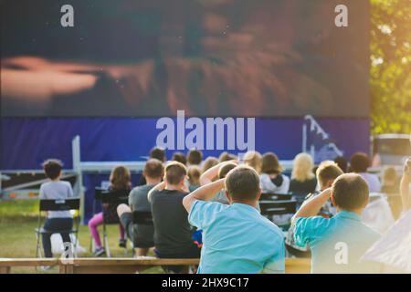 Un groupe de personnes regardant un écran de cinéma en plein air. Banque D'Images