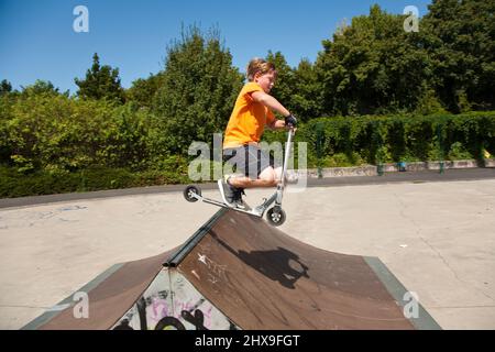 Boy saute avec un scooter sur une colonne vertébrale dans le skate parc et d'en profiter Banque D'Images