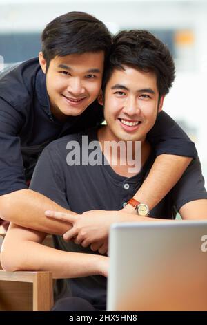 Le contenu juste pour être ensemble. Portrait d'un jeune couple gay affectueux se détendant à la maison avec un ordinateur portable. Banque D'Images