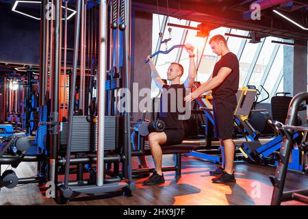 Un homme fort faisant des exercices lourds de dos dans la salle de gym sous la supervision d'un entraîneur professionnel. Un mode de vie sain Banque D'Images