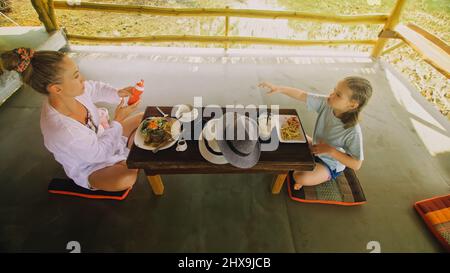 La famille heureuse mange et boit des boissons savoureuses en passant du temps dans le café flottant local sur l'eau.Mère et fille prenant le petit déjeuner à l'extérieur.Femme et Banque D'Images