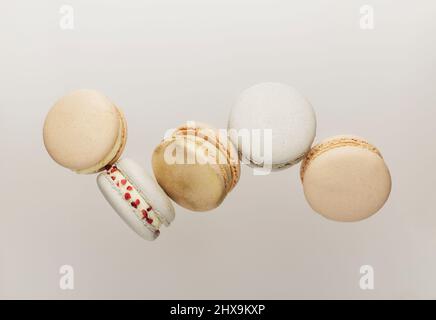 Cookies macaron blancs, jaunes, dorés volant, tombant en mouvement ou lévitant. Petits gâteaux de macaron français colorés et sucrés. Arrière-plan beige clair. Coupe brisée, pièces mordues, moitiés. Photo de haute qualité Banque D'Images