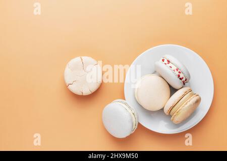 Biscuits macaron blanc, jaune, or. Petits gâteaux de macaron français colorés et sucrés. Arrière-plan jaune clair. Coupe brisée, pièces mordues, moitiés. Plaque blanche posée sur la table. Photo de haute qualité Banque D'Images