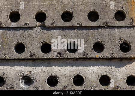 La texture linéaire des anciennes dalles de béton gris se bloque avec des trous empilés les uns sur les autres, vue de côté rapprochée. Matériau vieilli, construction. Banque D'Images