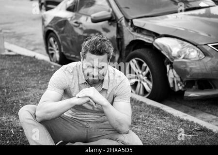 Contrarié triste conducteur assis sur la route à côté de la voiture brisée. Banque D'Images