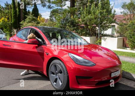 2022 rouge Tesla modèle 3 avec femme d'âge moyen, modèle sorti, en sortant de la voiture côté conducteur, Sydney, Australie Banque D'Images