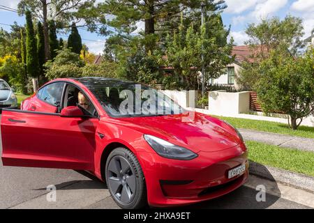 2022 rouge Tesla modèle 3 avec femme d'âge moyen, modèle sorti, en sortant de la voiture côté conducteur, Sydney, Australie Banque D'Images