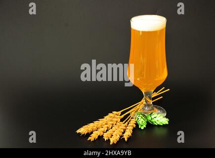 Grand verre de bière de blé avec mousse, houblon et oreilles sur fond noir. Positionnement vertical. Banque D'Images