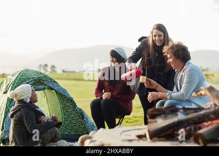 Vibes réfrigérées uniquement. Prise de vue d'un groupe de jeunes amis qui apprécient le café près du feu pendant un voyage de camping. Banque D'Images