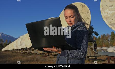 Une femme étudiante-opérateur de l'institut de physique terrestre solaire surveille les équipements de communication dans un ordinateur portable. Radiotélescope solaire à faisceau unique. DIM Banque D'Images