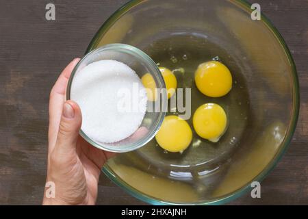 Femme à la main mettant le sucre dans les oeufs crus avant de battre Banque D'Images