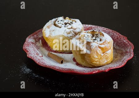 Deux pommes cuites ont rempli de l'avoine et sont poudrées de sucre en poudre sur une plaque rouge sur fond noir Banque D'Images