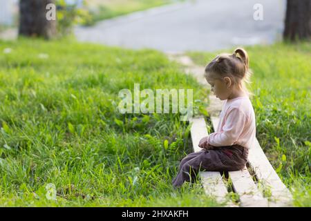 Triste petite fille assise sur le pont en bois avec des jambes bancales. Concept de tristesse et de solitude Banque D'Images