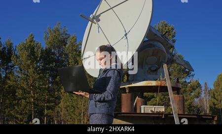 Une femme étudiante-opérateur de l'institut de physique terrestre solaire surveille les équipements de communication dans un ordinateur portable. Radiotélescope solaire à faisceau unique. DIM Banque D'Images