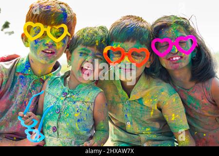 Groupe d'enfants joyeux avec des spectacles amusants criant à l'appareil photo après avoir joué avec de la poudre de holi colorée pendant la fête du festival. Banque D'Images