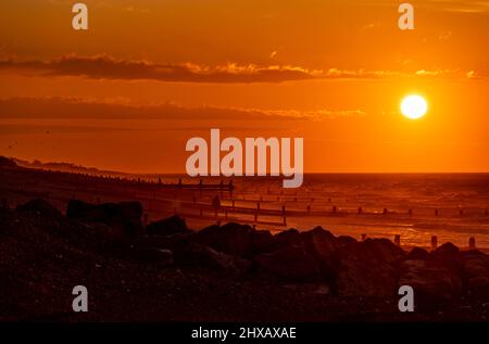 Rustington Beach, Royaume-Uni, 11th mars 2022. Le soleil se lève lorsqu'un chien promenant se promène le long de la plage de Rustington, dans le West Sussex. Crédit : Steven Paston/Alay Live News Banque D'Images