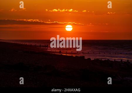 Rustington Beach, Royaume-Uni, 11th mars 2022. Le soleil se lève lorsqu'un chien promenant se promène le long de la plage de Rustington, dans le West Sussex. Crédit : Steven Paston/Alay Live News Banque D'Images