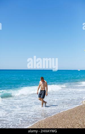 Jeune homme attrayant avec un beau corps en short marche le long de la plage de sable et de profiter des vacances d'été Banque D'Images