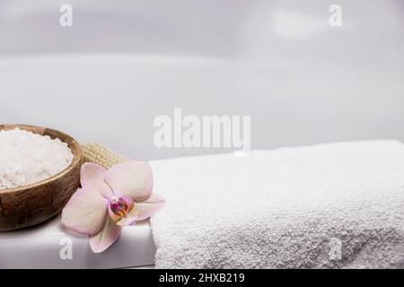 Préparation pour le soin spa de l'hôtel, la procédure de bain à la maison. Lavabo blanc dans la salle de bains, accessoires sur plateau brosse pour le pied ou le corps, serviette blanche, sel de mer dans un bol en bambou, fleur d'orchidée. Photo de haute qualité Banque D'Images