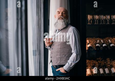 beau homme avec un verre de vin debout près d'un rack d'échantillons de vin. Banque D'Images