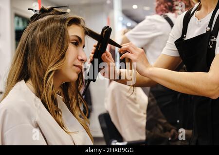Styliste professionnelle peignant les cheveux d'une jeune femme cliente dans le salon de beauté. Banque D'Images