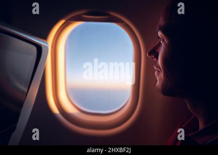 Portrait de l'homme voyageant en avion. Passager regardant à travers la fenêtre de l'avion pendant le vol au lever du soleil. Banque D'Images
