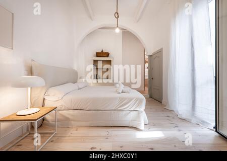 Belle chambre avec un très grand lit, parquet en pin clair, rideaux blancs et une poitrine semi-circulaire d'un côté de la chambre Banque D'Images