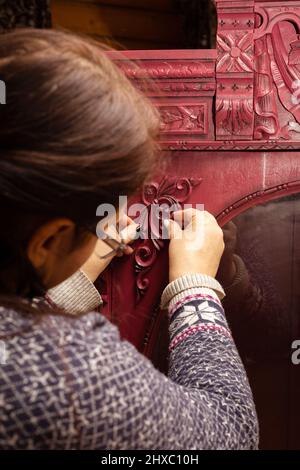 Vieille femme mains accrochent des ornements sculptés à bois rouge clair carton couleur avec le verre rond en face dans la maison de chalet en bois. Réutilisation des objets anciens Banque D'Images