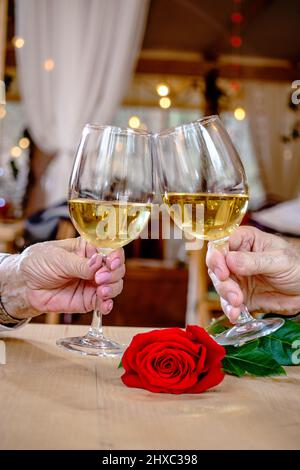 Mains d'un couple romantique âgé, tenant des verres avec du vin, en grillage et en trinking avec eux sur une rose rouge. Toast de mariage. Banque D'Images