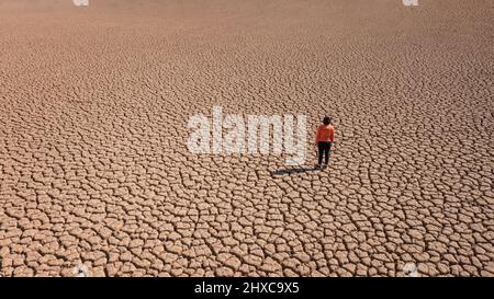 Silhouette d'un homme sur une terre sablonneuse craquée vide non fertile pendant une sécheresse. Le concept de catastrophe écologique sur la planète. Banque D'Images