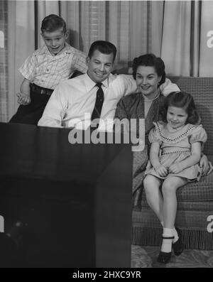 Famille bien habillée de maman, papa, garçon et fille assis sur le canapé regardant la télévision Banque D'Images