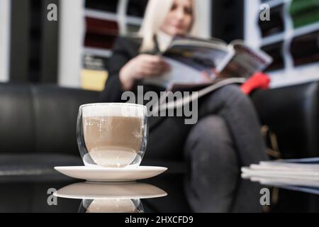 Une fille dans un concessionnaire de voiture boit le café et lit la presse. Gros plan du café. Banque D'Images