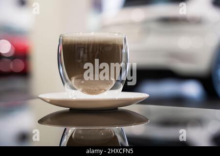 Tasse de cappuccino avec mousse sur une table en verre noir dans un concessionnaire automobile. Banque D'Images
