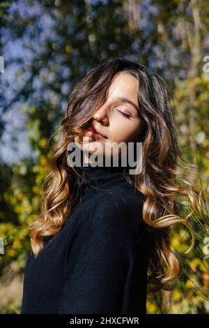 Jeune femme profitant de la journée ensoleillée avec les yeux fermés Banque D'Images