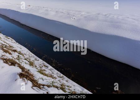 Petite rivière étroite en hiver, beaucoup de neige sur la rive Banque D'Images