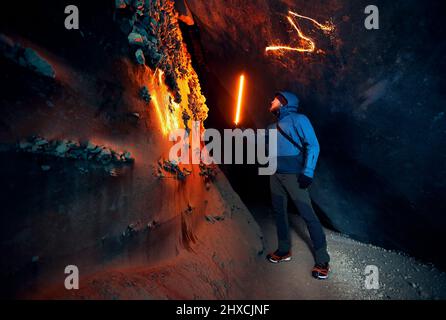 Homme de tourisme tenant une lampe lumineuse rouge dans une profonde grotte de glace glaciaire étroite avec explorer le glacier de montagne d'hiver au Kazakhstan Banque D'Images