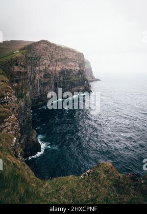 Larges falaises vertes sur les îles Féroé avec des vagues qui frappent la ligne de rivage Banque D'Images