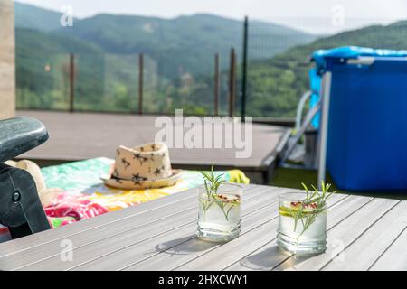 Chaise longue avec chapeau et deux cocktails sur une table à côté d'une piscine portable Banque D'Images