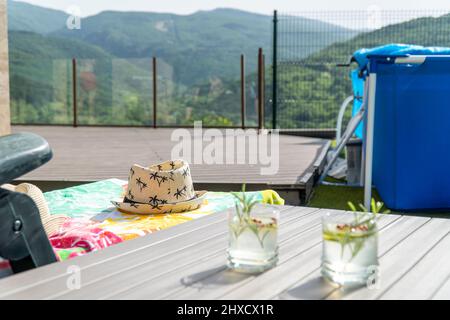 Chaise longue avec chapeau et deux cocktails sur une table à côté d'une piscine portable Banque D'Images