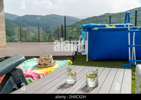 Chaise longue avec chapeau et deux cocktails sur une table à côté d'une piscine portable Banque D'Images