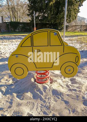 Une balançoire à ressort en forme de voiture stylisée sur une aire de jeux vide pour enfants avec un sol sablonneux Banque D'Images