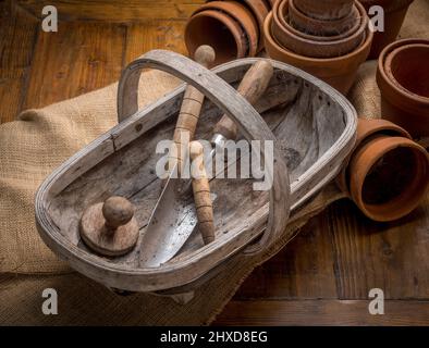 Pots de plantes en terre cuite recouverts de toile d'araignée avec tapis en bois traditionnel contenant une truelle, un damper et un dameur, au premier plan. Banque D'Images