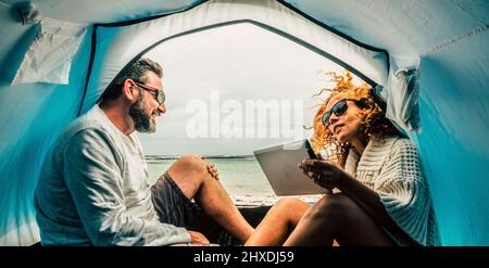 Couple d'adultes caucasiens souriez et profitez de loisirs à l'intérieur d'une tente en camping gratuit à la plage avec vue sur la mer. Concept de tourisme alternatif et de voyage vac Banque D'Images