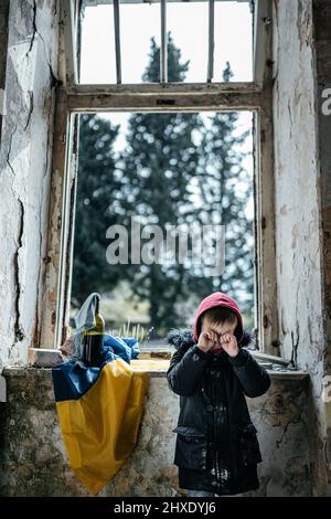 Petit garçon dans une guerre de maison ruinée en Ukraine drapeau ukrainien Banque D'Images