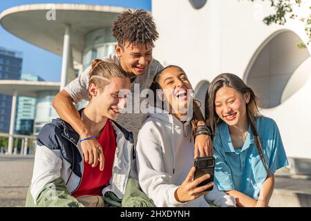 Des amis adolescents heureux regardant le téléphone portable et riant dans la rue de la ville. Concept de technologie pour les jeunes. Banque D'Images