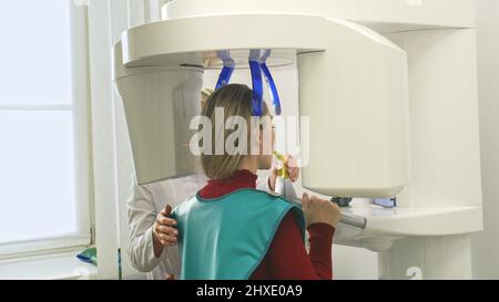 Médecin pour prendre une image scanner 3D tomographie des dents et de la mâchoire dans la clinique dentaire de laboratoire moderne. Une infirmière féminine montre à la patiente une machin à rayons X. Banque D'Images